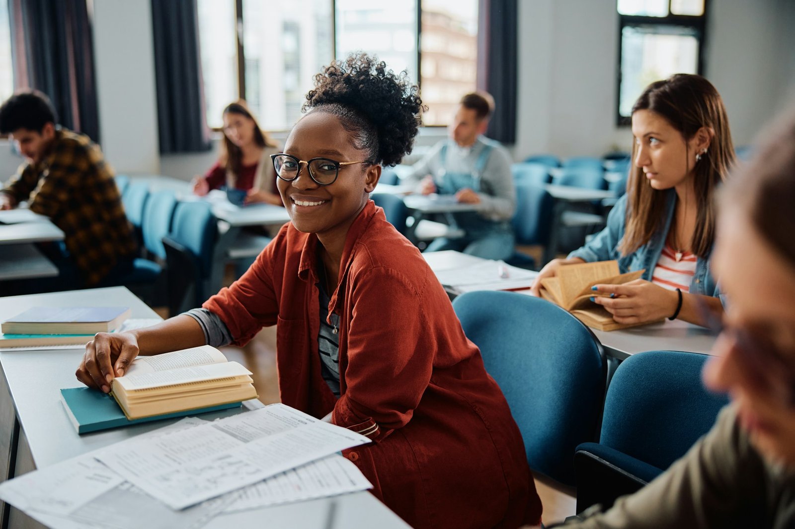 Happy black woman studying during a class in lecture hall and looking at camera.